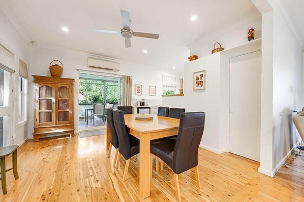 A dining area with a wooden table and chairs, a ceiling fan, and a view of the outdoors.