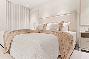 A bed with a quilted white cover, a beige throw blanket, and several pillows.