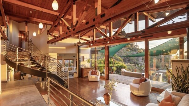 Un amplio salón con una escalera moderna, ventanas grandes y vistas al exterior.