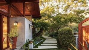 Un sendero conduce a una casa con terraza de madera y una planta en maceta.