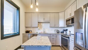 Una cocina moderna con armarios blancos, electrodomésticos de acero inoxidable, encimera de granito y una ventana con persianas.