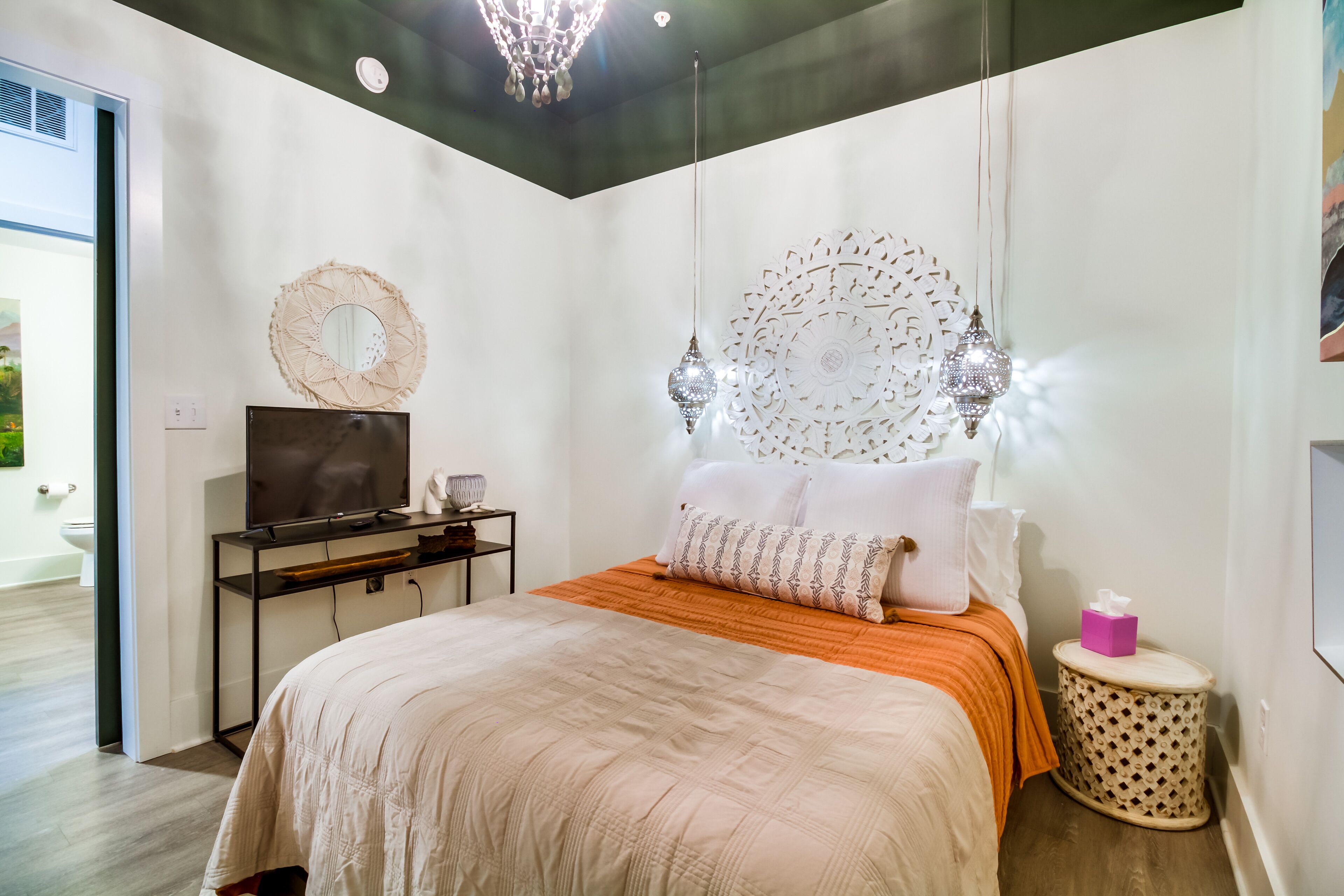A modern bedroom with a bed, a TV, decorative wall art, and a unique ceiling light fixture.