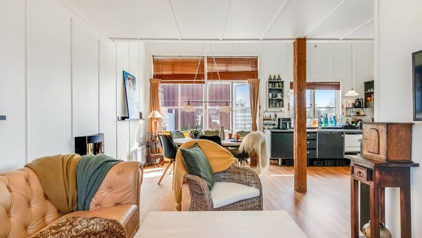 Ein geräumiges Wohnzimmer mit einer Couch, Sesseln, einem Couchtisch und einer Küchenzeile im Hintergrund.