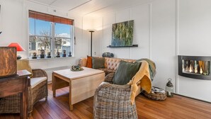 Ein Wohnzimmer mit einer Couch, einem Tisch, Korbmöbeln, einem Kamin und einem Fenster mit Jalousien.