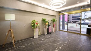 Un hall d’entrée doté d’un sol en marbre, d’un lampadaire et de trois plantes en pot décorées de rubans.