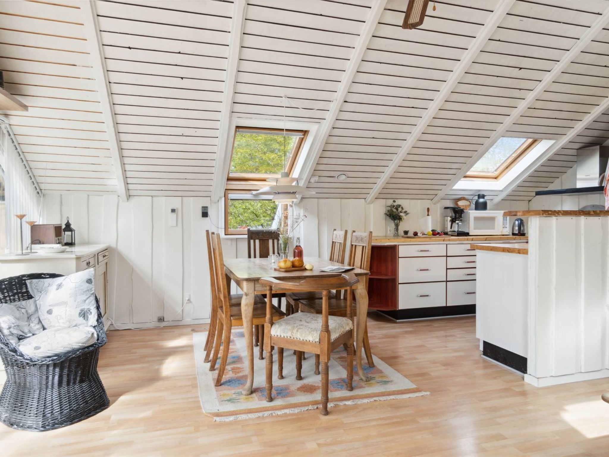 Une cuisine chaleureuse avec un coin repas, comprenant une table en bois, des chaises et un fauteuil en osier.