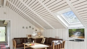A cozy living room with a sloped ceiling, a wooden table, a brown sofa, and a television on the wall.