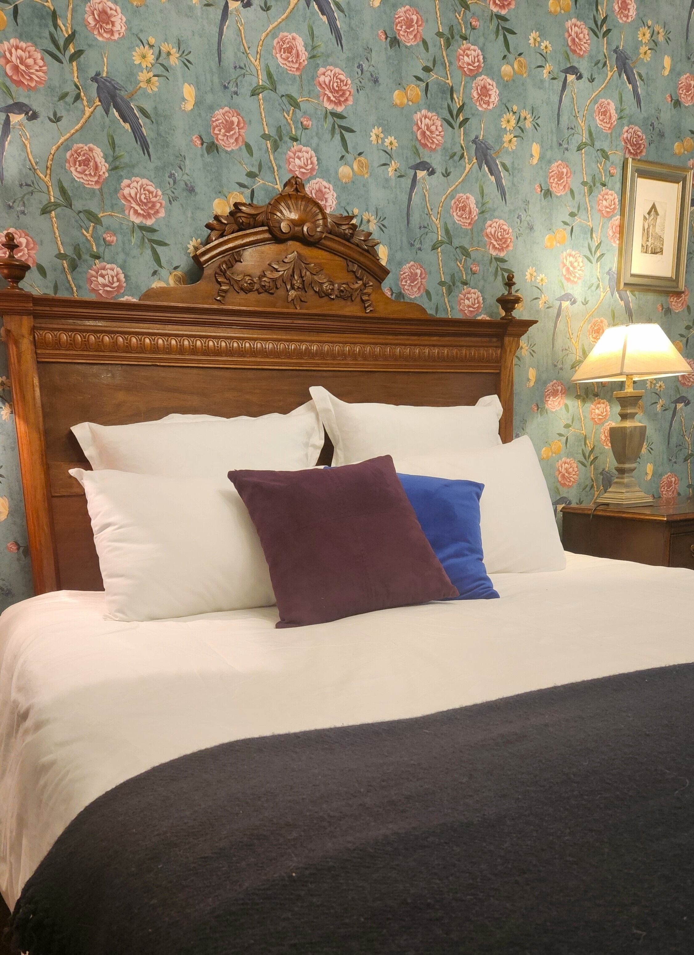 A bed with a wooden headboard, white and purple pillows, and a dark blue bedspread.