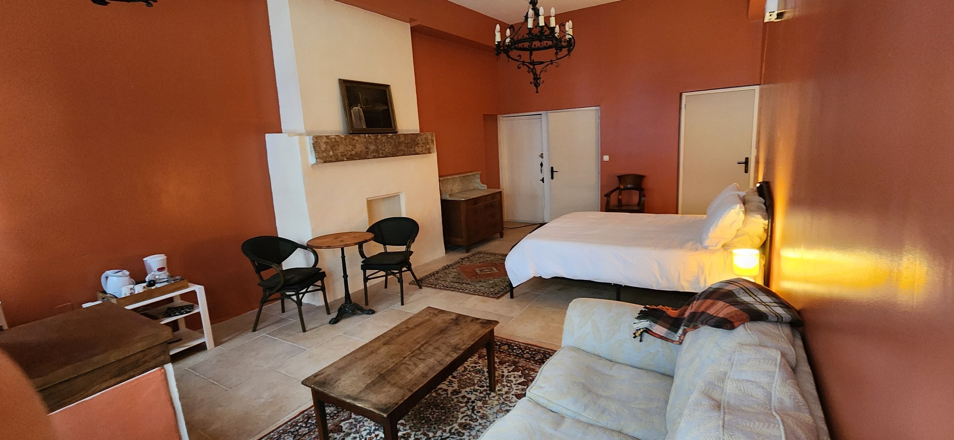 Un cuarto acogedor con cama, sofá, una mesita y una silla. Hay una chimenea, un armario y un espejo en la pared.
