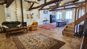 Un amplio salón con vigas de madera a la vista, un tapete grande y decorado, un sofá y una mesa de comedor.