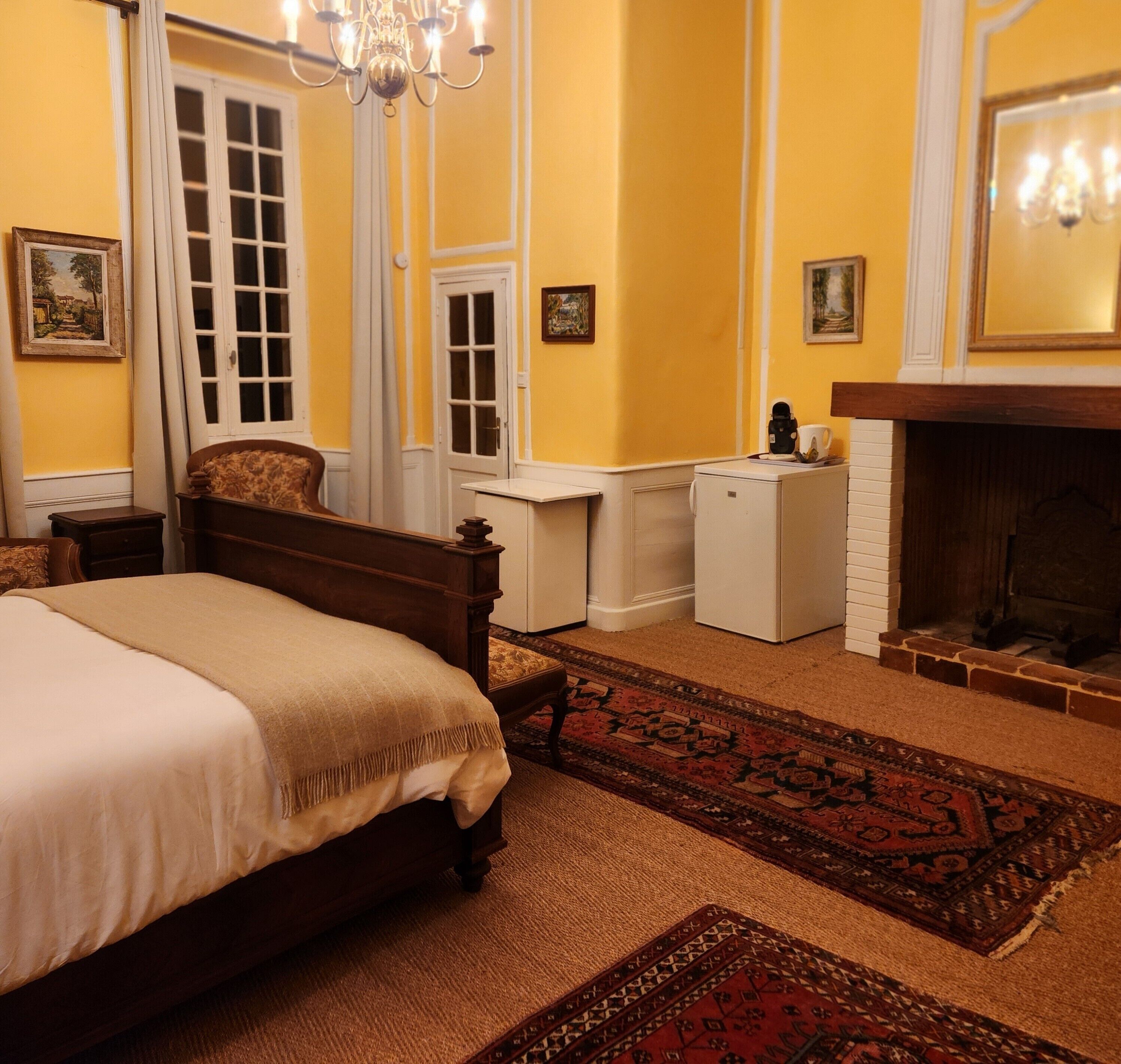 Un dormitorio con cama, un pequeño armario blanco, una chimenea y un espejo grande.