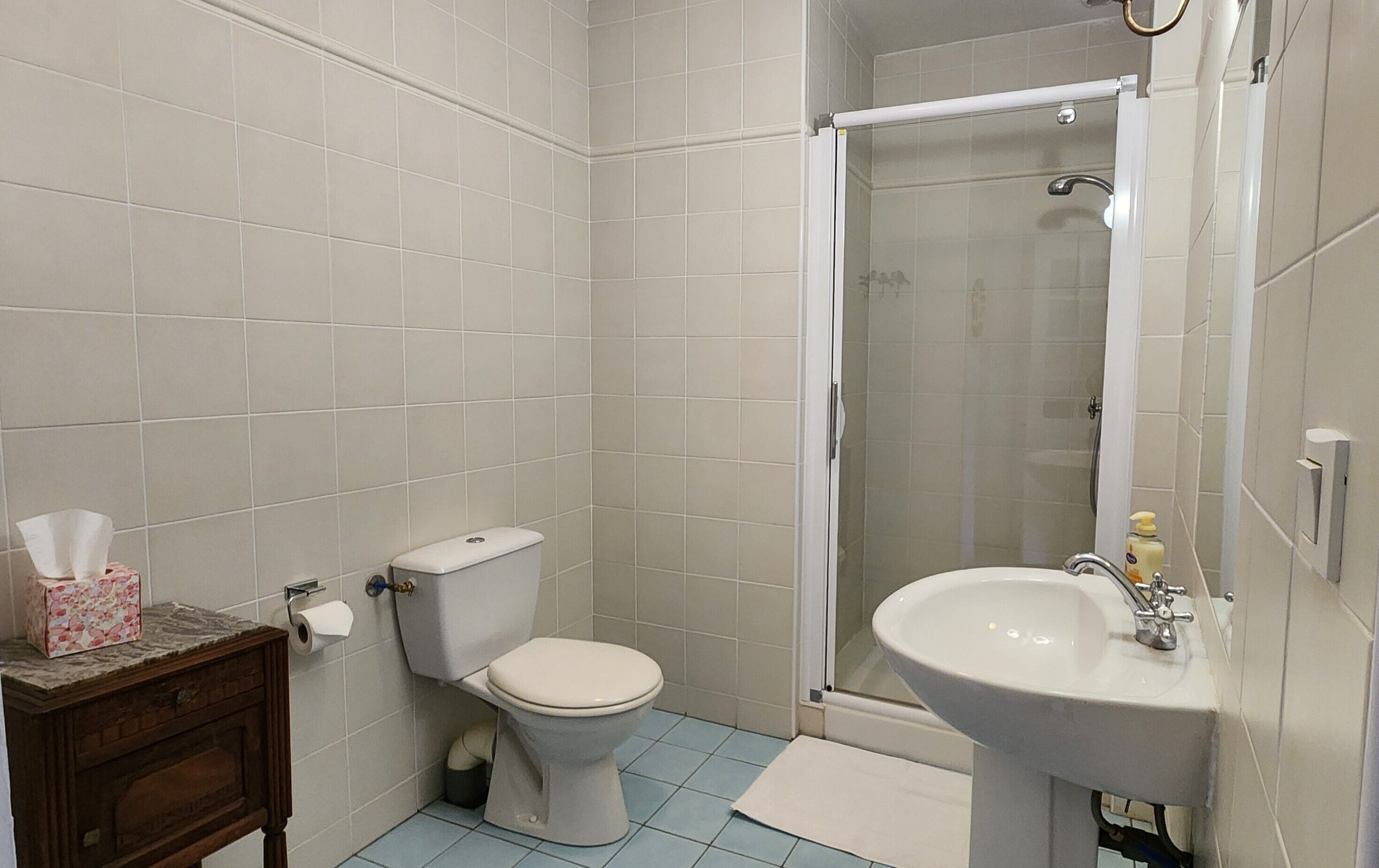 Un baño con inodoro, ducha, lavamanos y un armario de madera con caja de pañuelos.