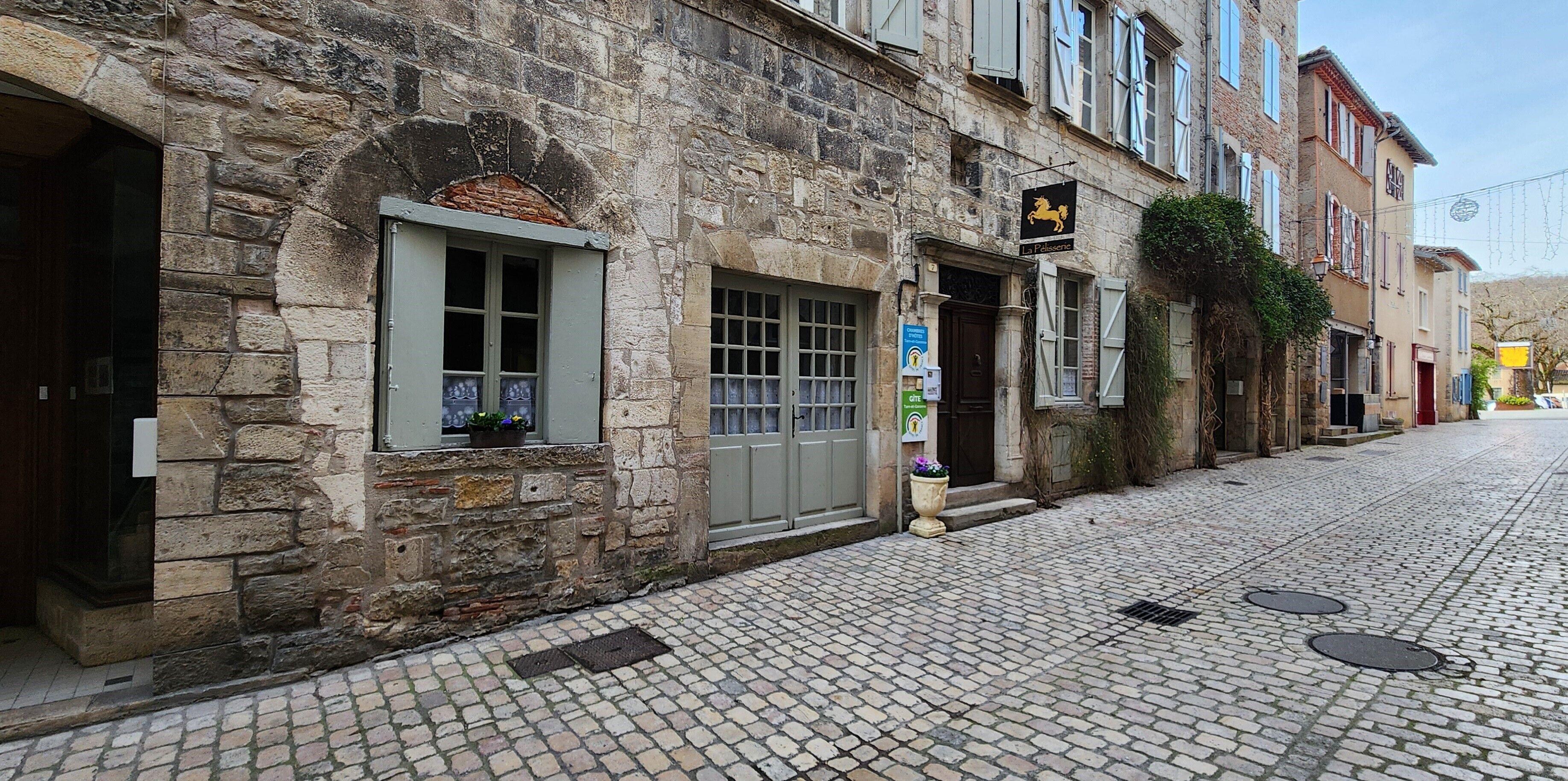 A stone building with a traditional European architectural style, featuring a cobblestone street and a sign indicating a local business.