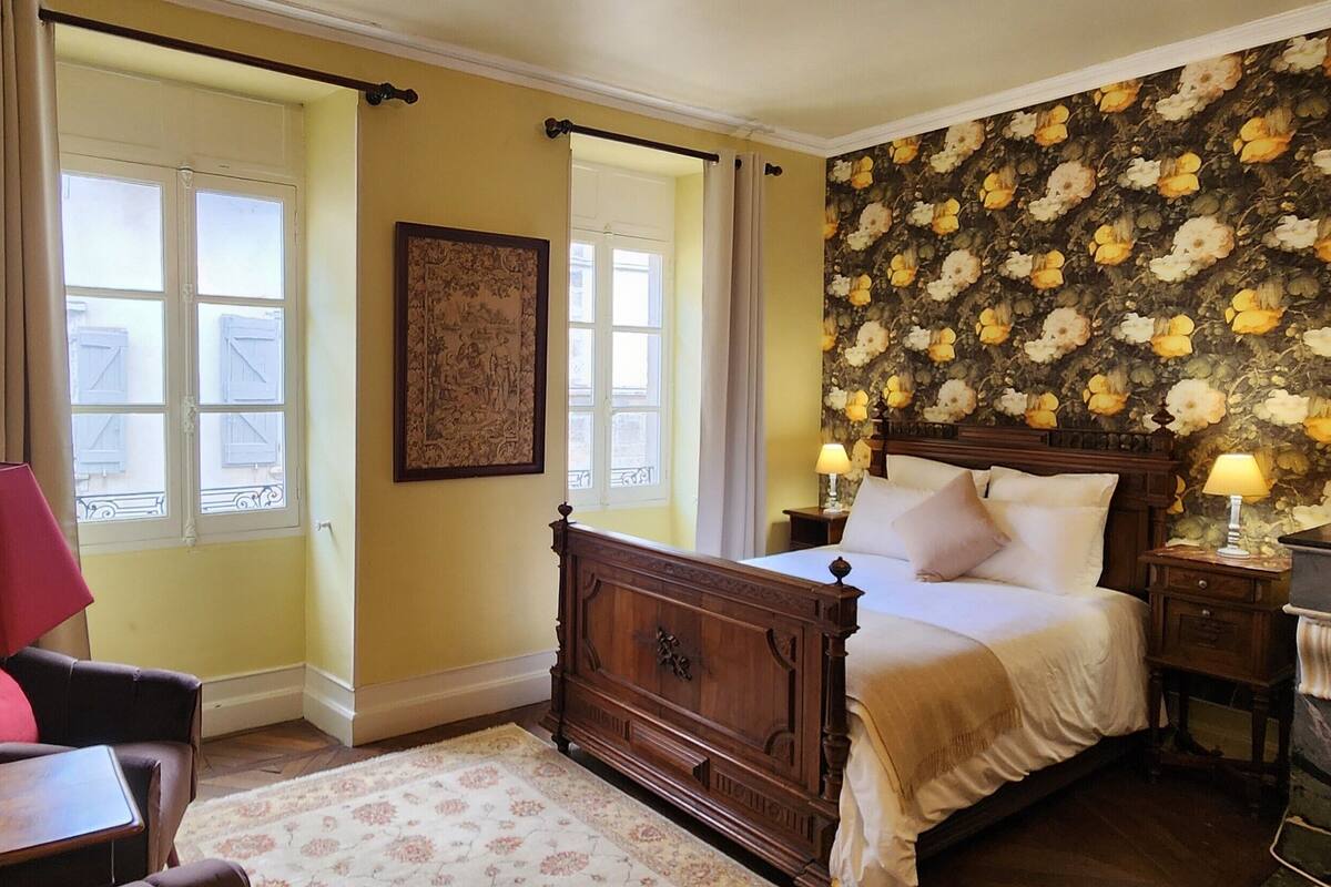 Une chambre à coucher avec un lit, une table de chevet, une lampe, une chaise et une fenêtre.