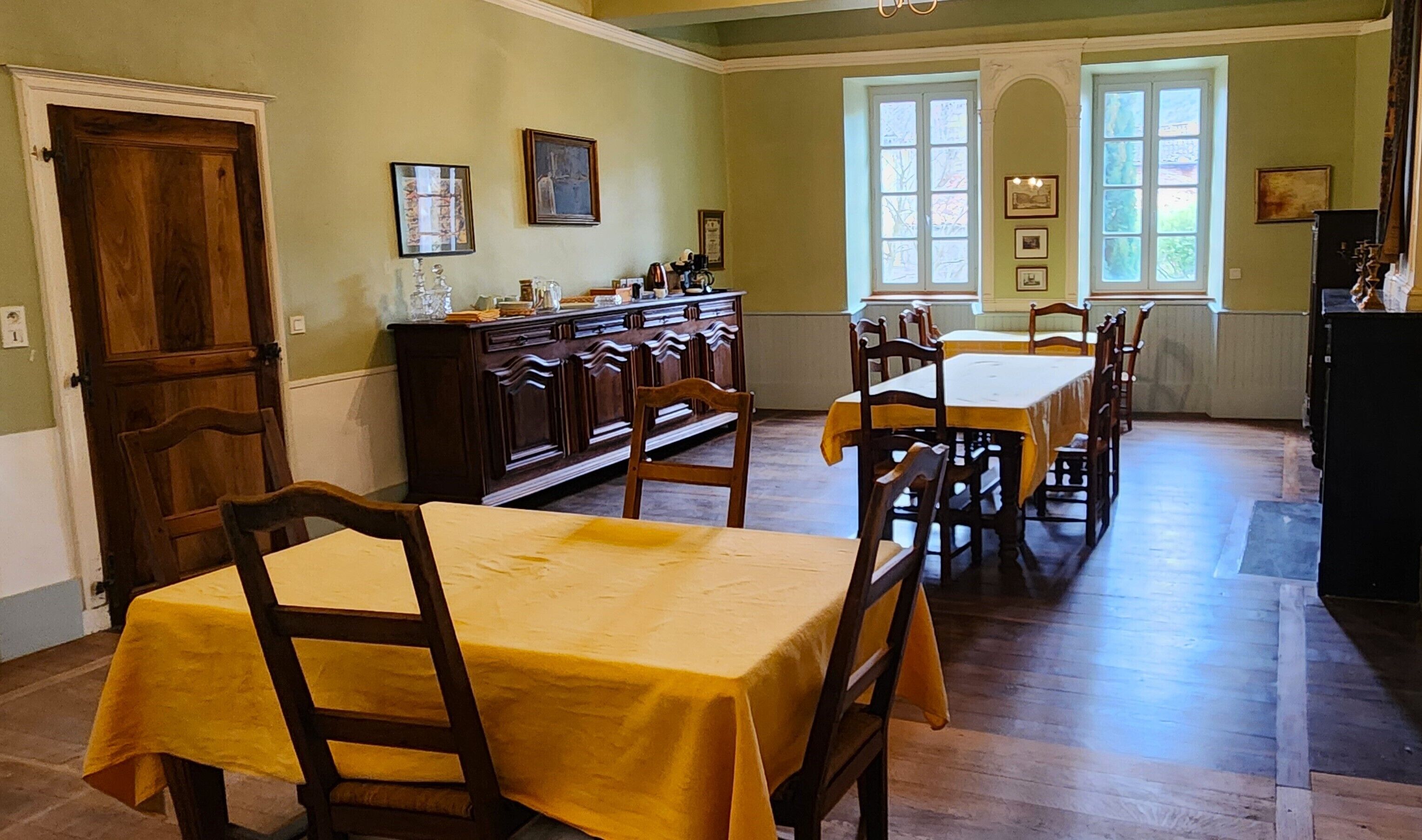 A dining room with wooden tables and chairs, a dark wooden cabinet, and framed pictures on the walls.