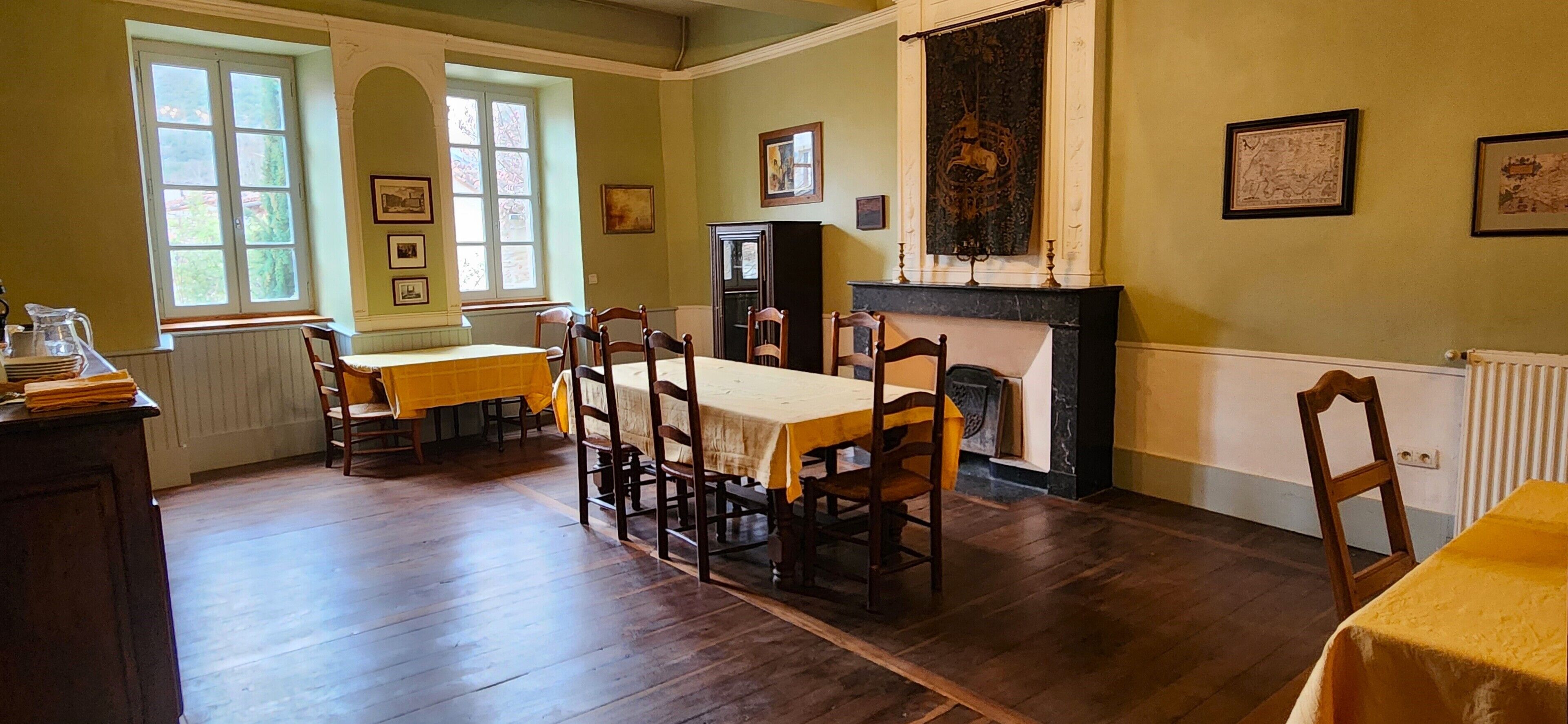 A dining room with a wooden table and chairs, a fireplace, and framed pictures on the walls.