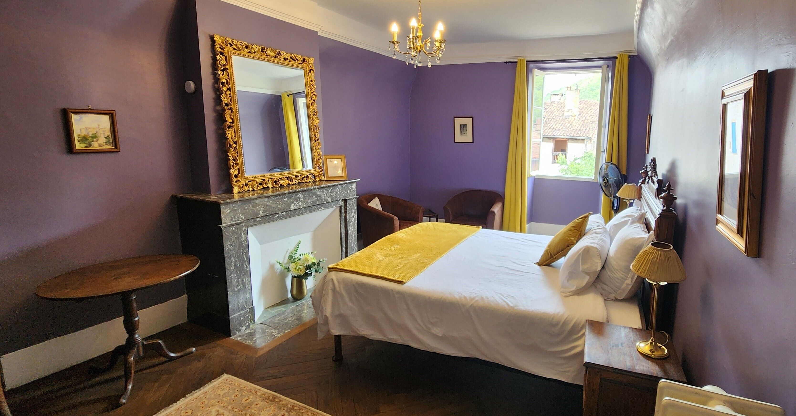 Une chambre à coucher avec un lit, une cheminée, un miroir et une fenêtre avec des rideaux.