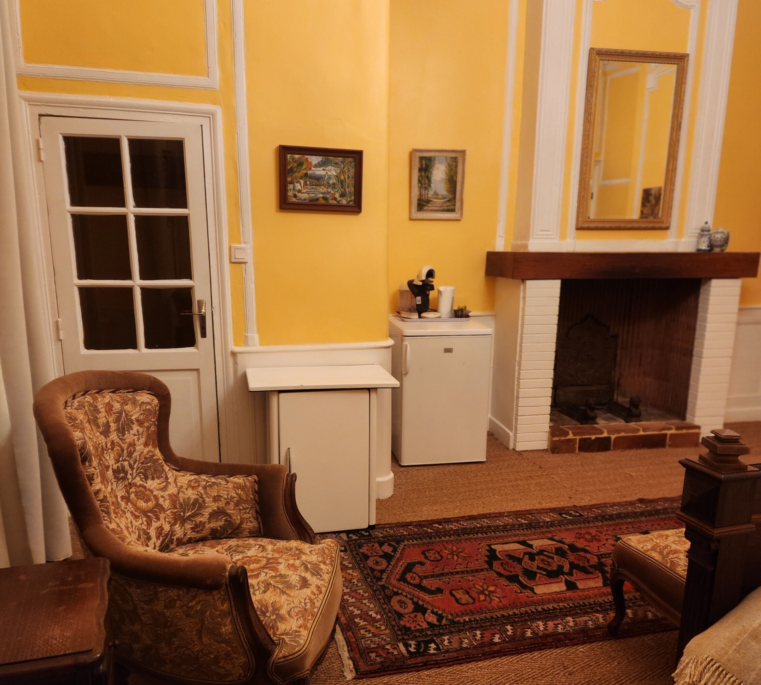 A room with a patterned armchair, a small white cabinet, a fireplace, and a rug.