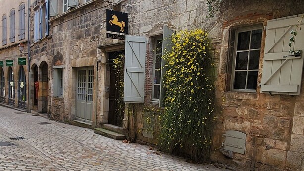 Una calle empedrada con edificios históricos de piedra, contraventanas y un cartel de restaurante El Caballo Negro.