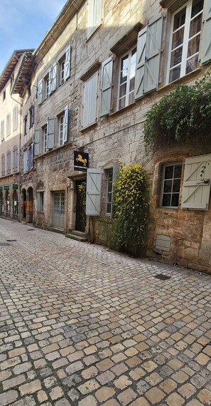 Une rue pavée bordée de bâtiments historiques en pierre, avec des volets et une enseigne indiquant un restaurant appelé «Le Cheval Noir».