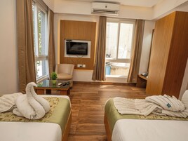 A hotel room with two beds, a TV, a chair, a small table, and a window with curtains.