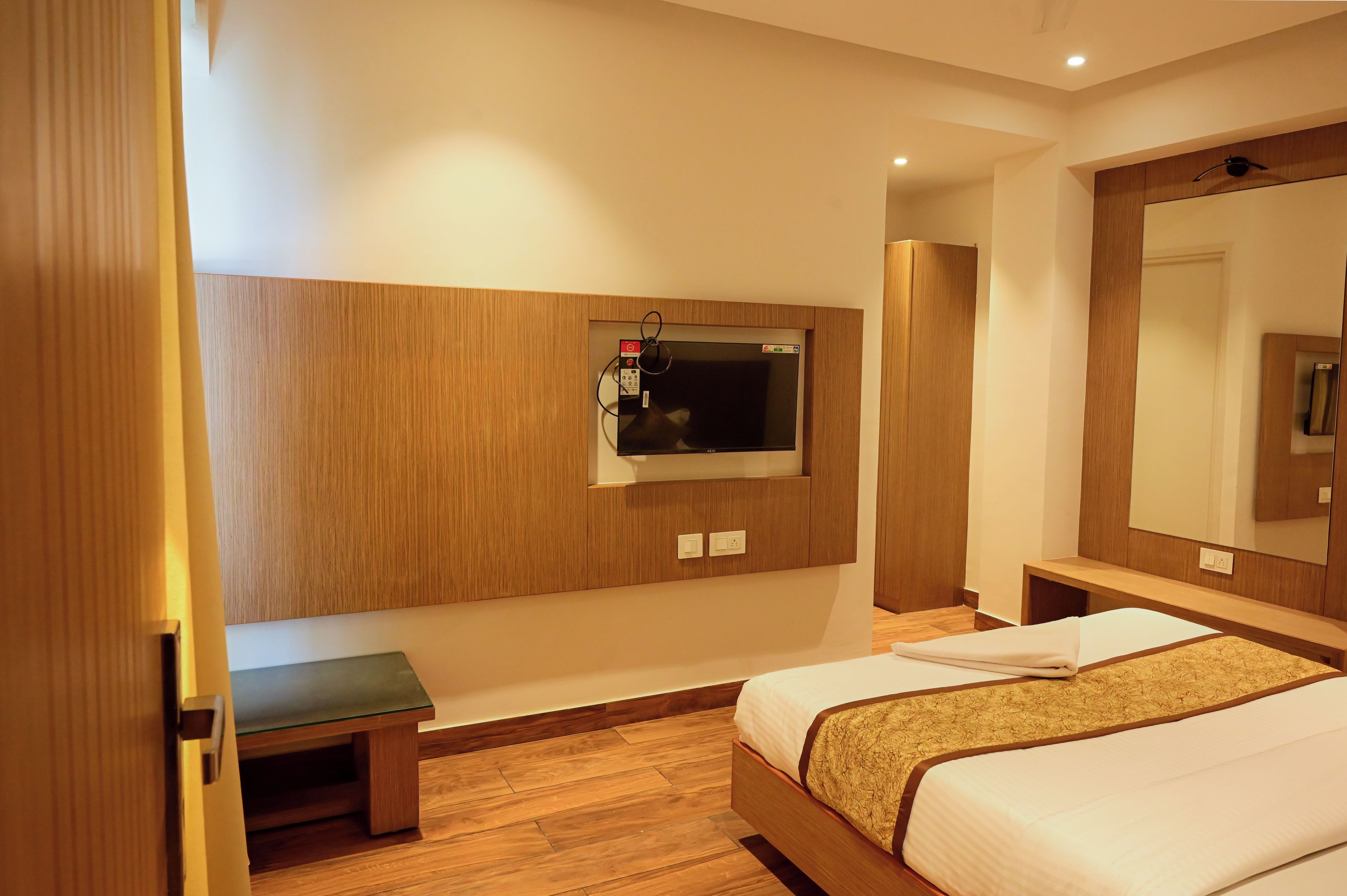 A hotel room with a bed, a bench, a TV mounted on the wall, and a mirror.