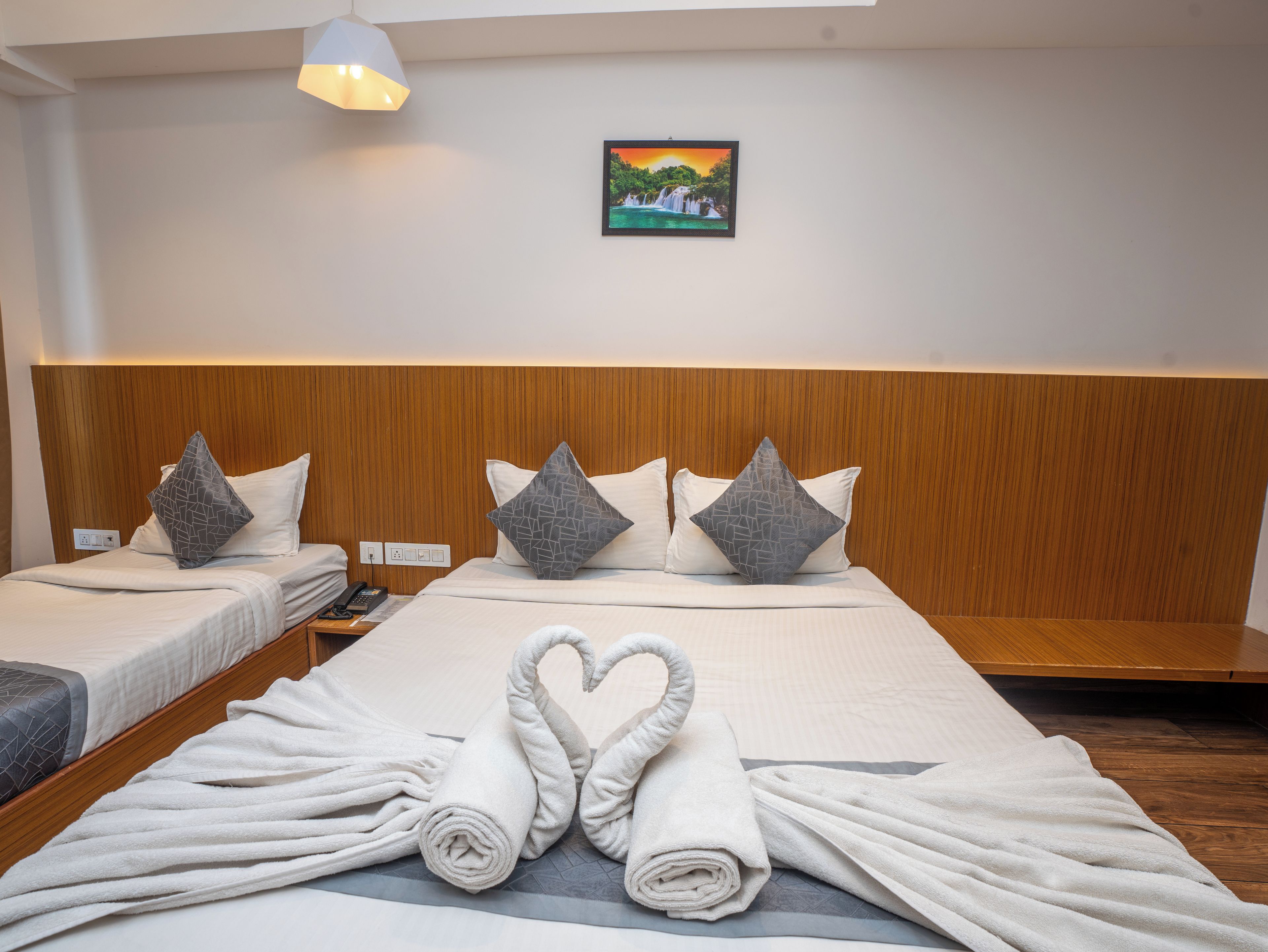 A hotel room with a large bed, two bedside tables, a wall-mounted painting, and a ceiling light.