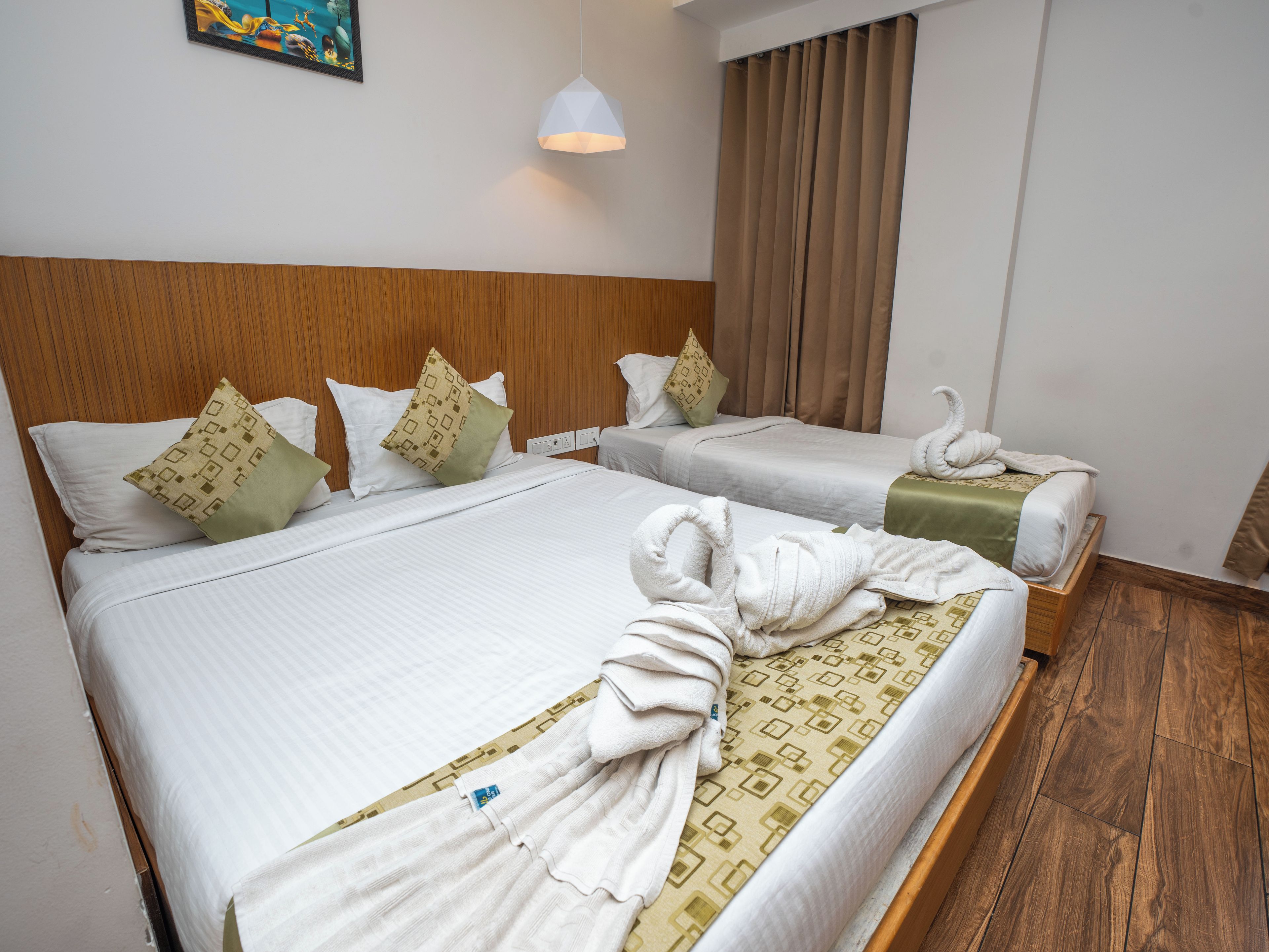 A hotel room with two beds, wooden headboards, white bedding, patterned pillows, a wall-mounted light, and a window with curtains.