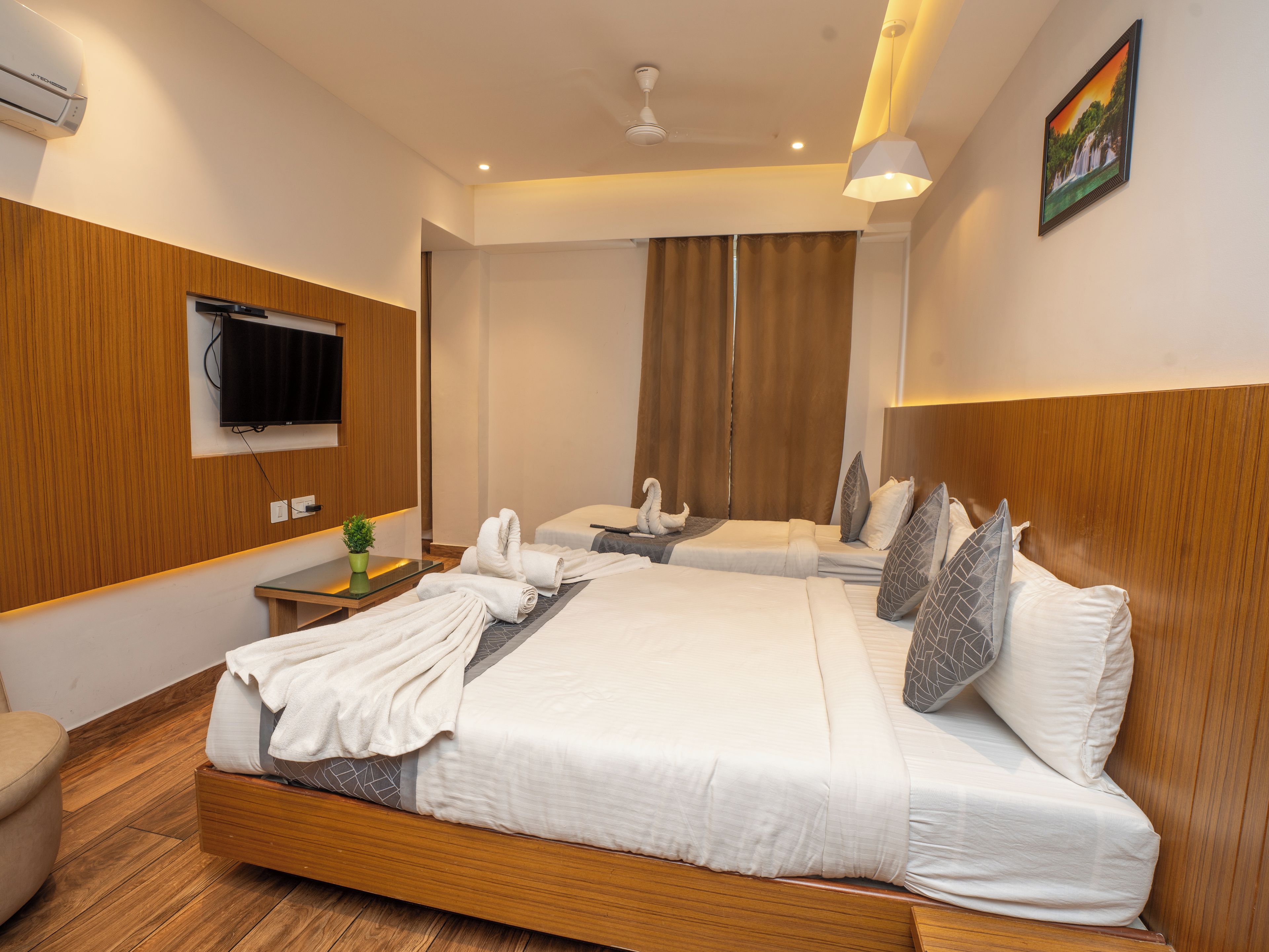A hotel room with a large bed, a television, a flat-screen TV mounted on the wall, a ceiling fan, and a painting on the wall.