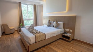 Habitación de hotel moderna con una cama grande, una mesita de noche, una silla y un ventanal con cortinas.