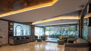 Un vestíbulo amplio con diseño moderno, que incluye una zona de estar con sofás y sillones, una mesa de centro y una planta decorativa.