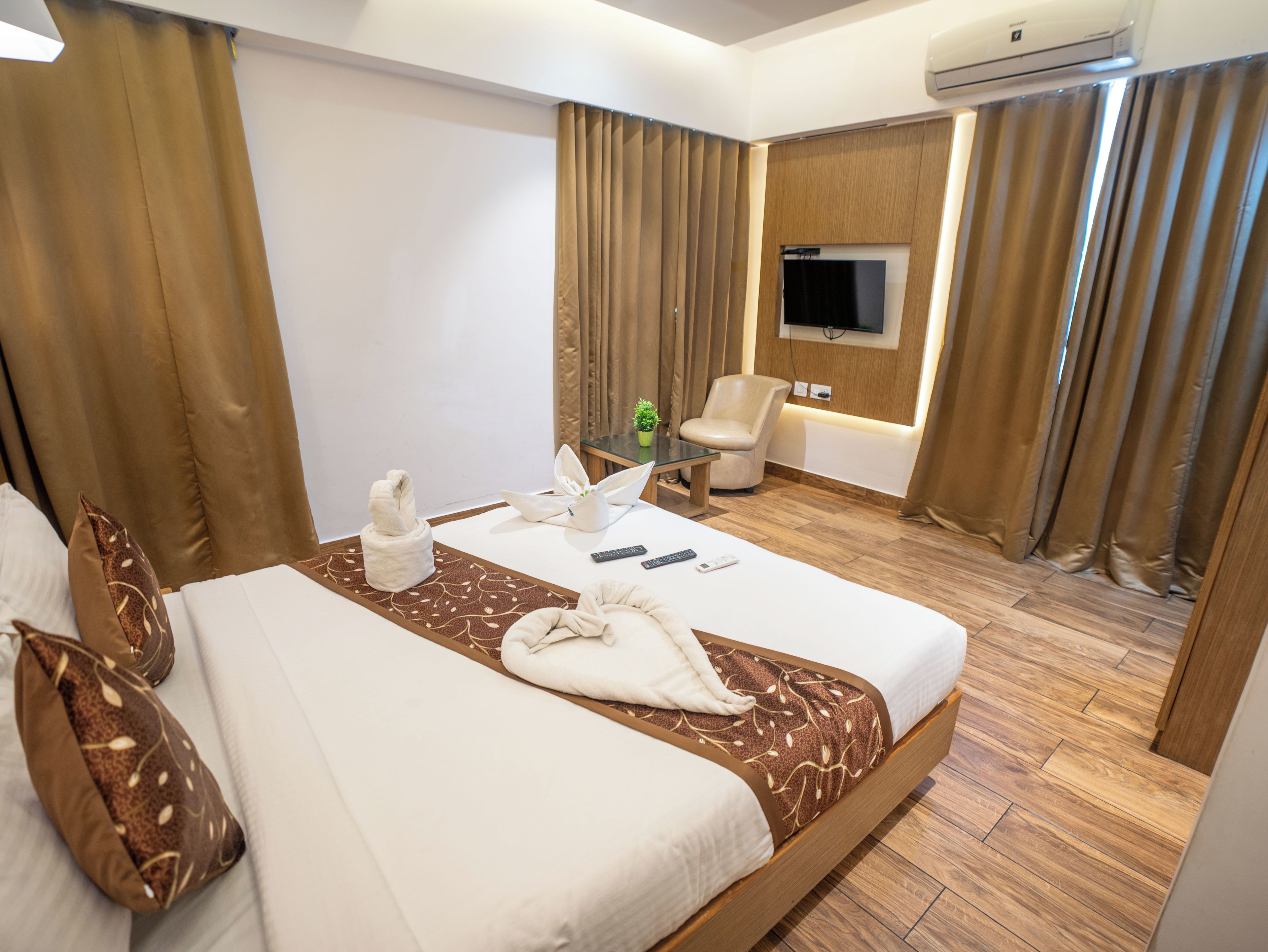 A hotel room with a bed, a chair, a TV, and an air conditioning unit.