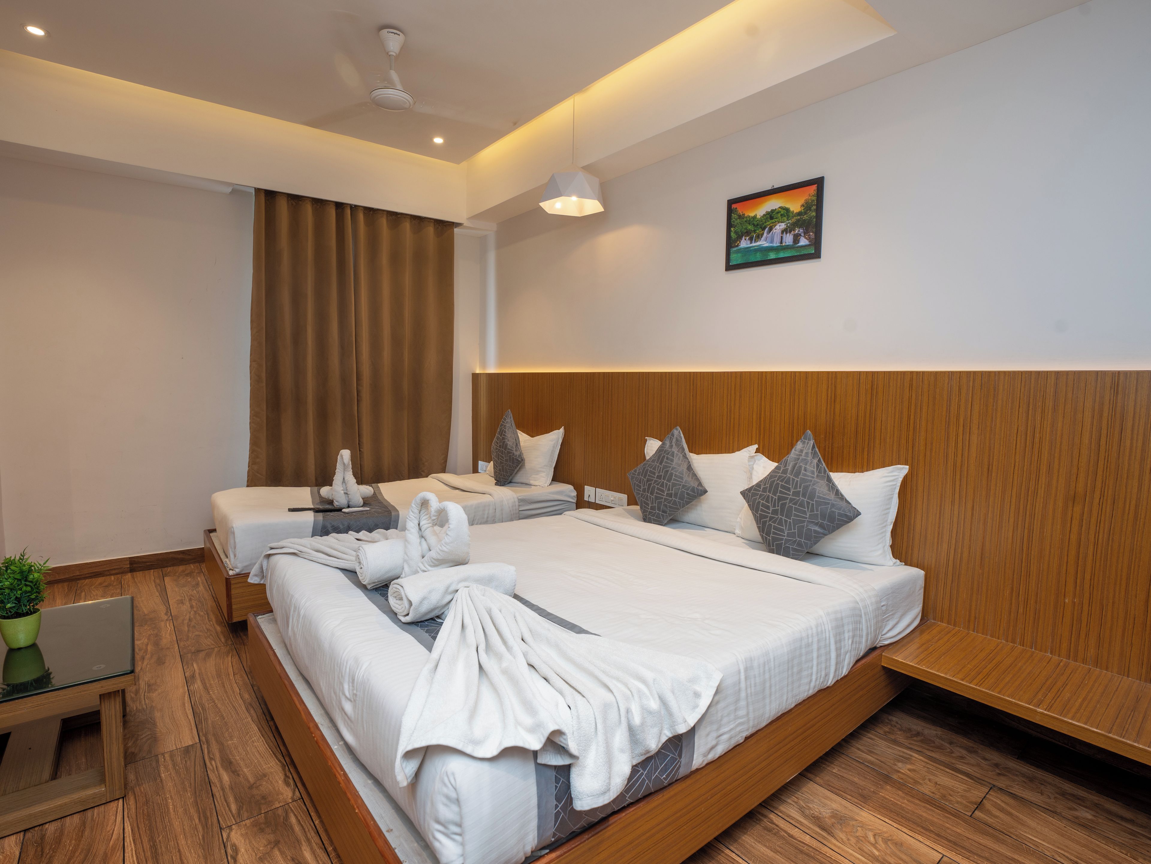 A hotel room with a large bed, a smaller bed, a desk with a laptop, and a potted plant.