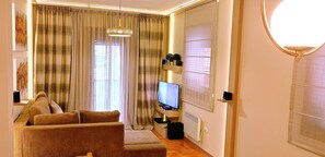 Ein Wohnzimmer mit einer Couch, einem Fernseher und einem Fenster mit Vorhängen.