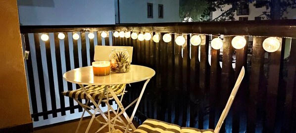 Ein kleiner runder Tisch mit Kerze und Glas, vor einem dunklen Holzschienendach und Lichterkette.