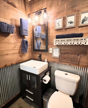 A bathroom with a wooden wall, a white sink, a black cabinet, a toilet, and framed pictures.