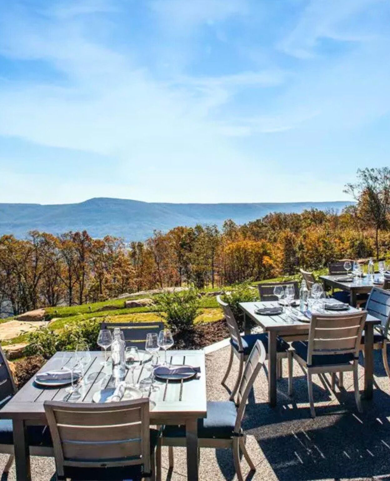 An outdoor dining area with tables set for two, overlooking a scenic view of trees and hills.
