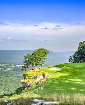 A golf course with a clear view of the surrounding landscape, including trees and distant hills.