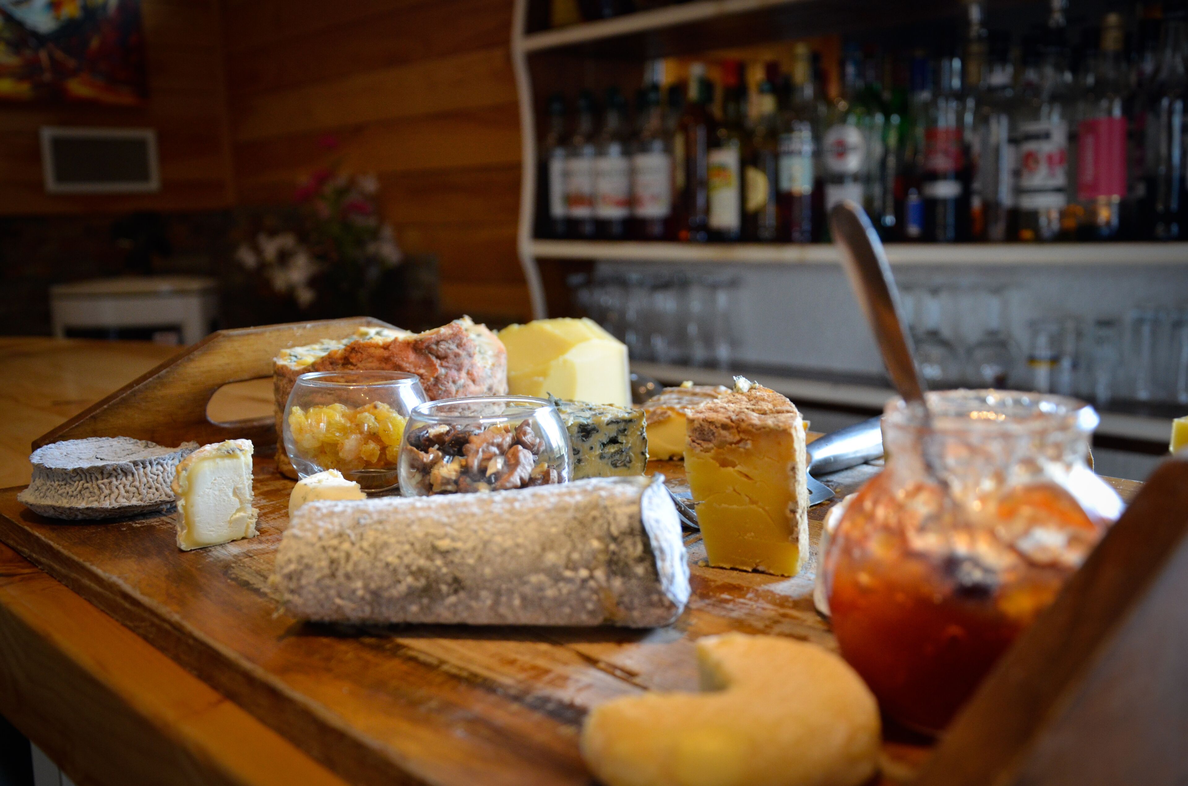 A variety of cheeses and jams on a wooden counter in a bar setting.