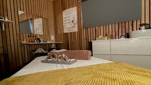 Une chambre avec un mur recouvert de panneaux de bois, un lit avec une couverture jaune, une table de chevet avec des articles de toilette, un miroir et une affiche accrochée au mur.