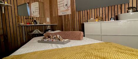A bedroom with a wooden panel wall, a bed with a yellow blanket, a bedside table with toiletries, a mirror, and a poster on the wall.