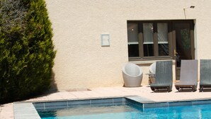Une piscine avec une terrasse en bois, un patio couvert avec des chaises et un bâtiment doté d’un toit en tuiles.
