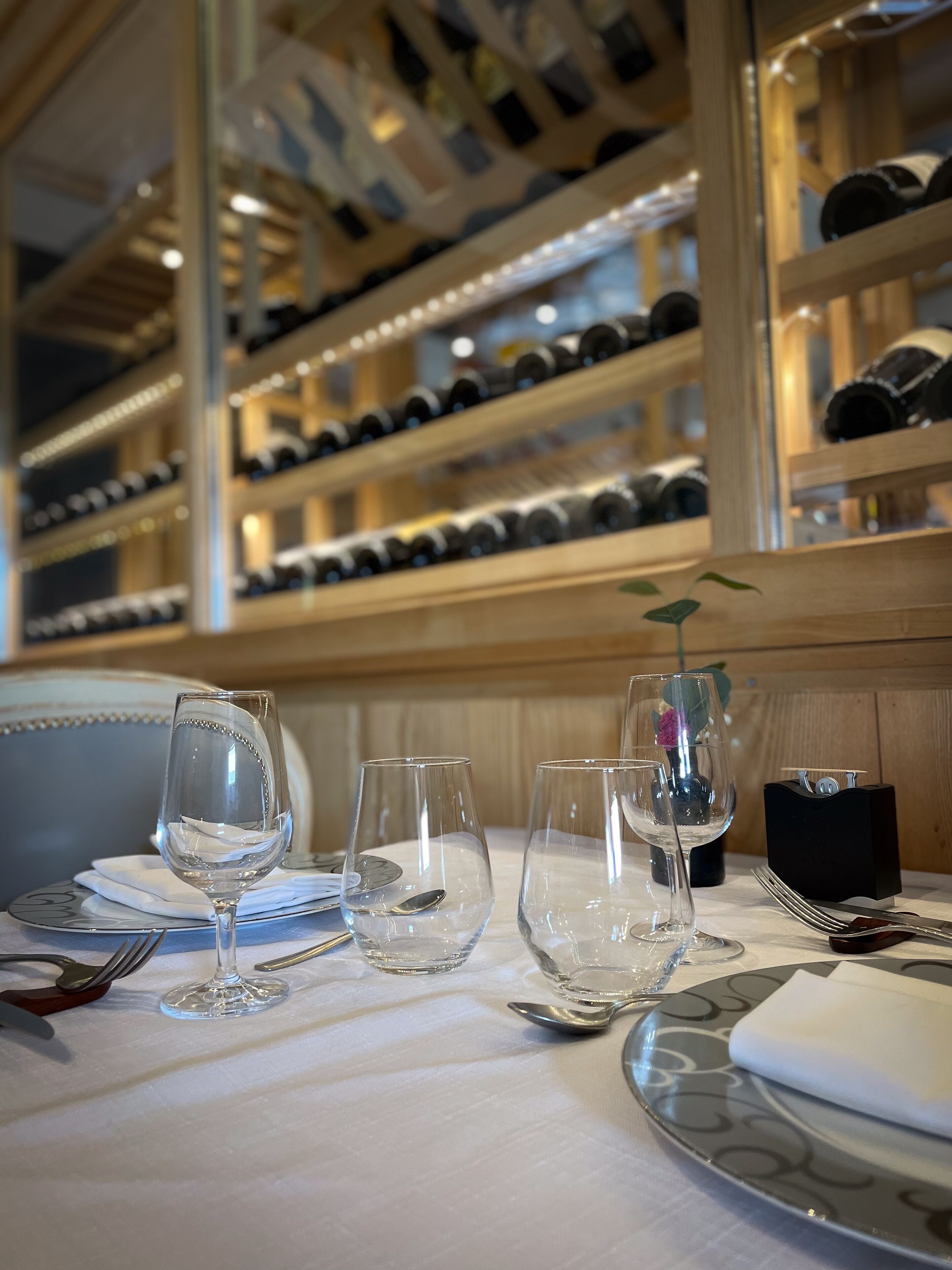 Una mesa dispuesta para comer, con copas de vino, cubiertos y un pequeño jarrón con una flor.