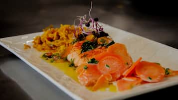 A white rectangular plate with a piece of salmon, a side of what appears to be sautéed vegetables, and a garnish of purple sprouts.