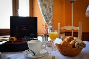 A breakfast setting with a coffee cup, a glass of orange juice, a basket of bread, and a box of Folletis chocolates.
