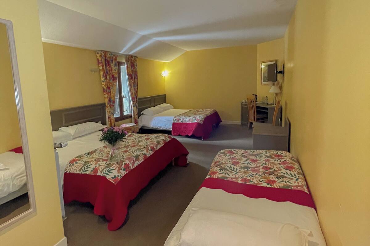 Une chambre d’hôtel avec deux lits, un miroir, une table de chevet et une fenêtre avec des rideaux.