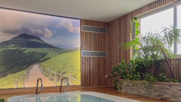 Une piscine intérieure moderne, dotée d’une terrasse en bois et offrant une vue panoramique sur un paysage montagneux.