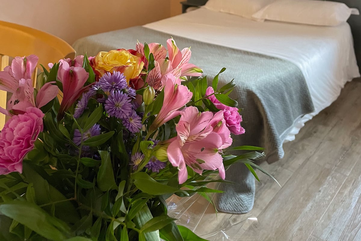 Une chambre d’hôtel avec un lit, une table de chevet et un vase de fleurs.