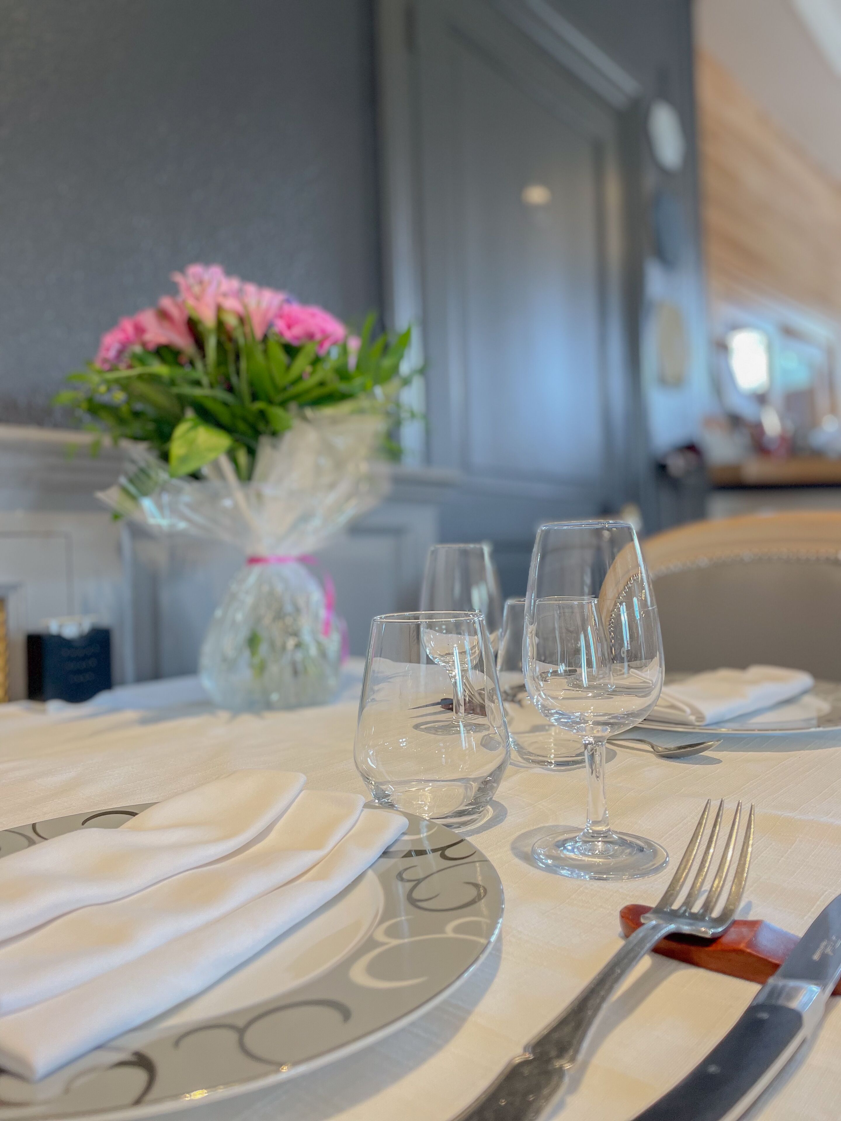 A dining table set with white tablecloths, clear wine glasses, and silverware.