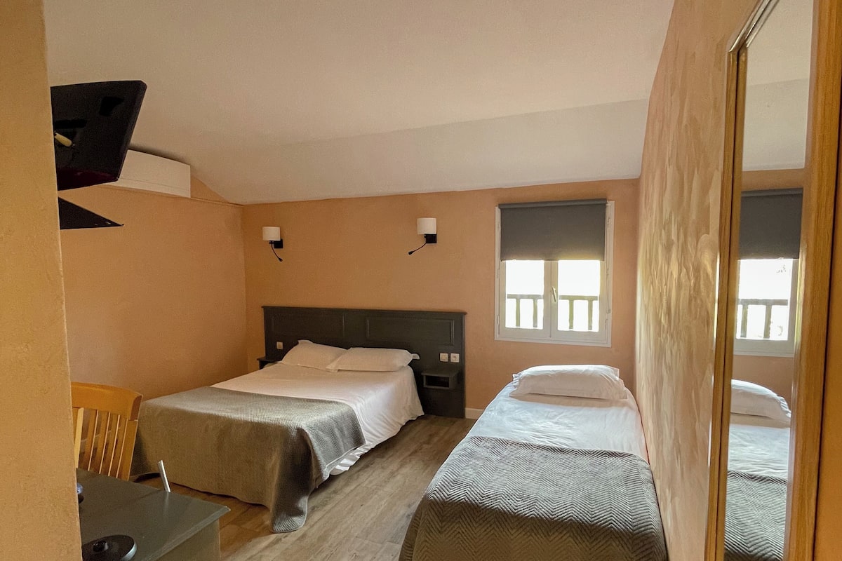 Une chambre d’hôtel de taille modeste, équipée de deux lits simples, d’un bureau avec une chaise, d’une petite table et d’un miroir.